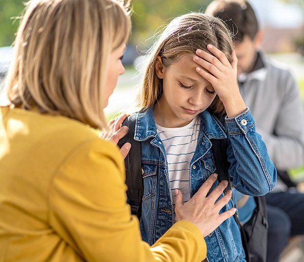 Worried adult comforts upset child outside school, illustrating peer challenges and emotional distress addressed through assessment.