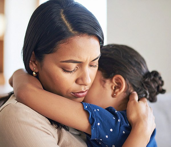 Worried caregiver hugs anxious child, illustrating emotional behaviors like anxiety or withdrawal explored through assessment.