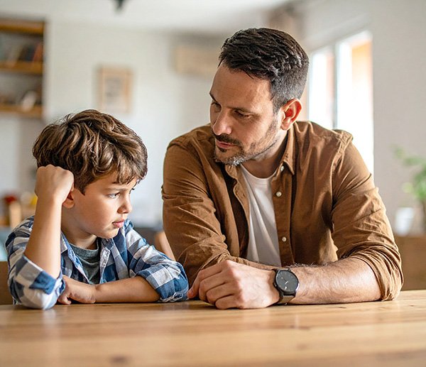Concerned parent talking with frustrated child at table, reflecting parenting challenges and need for assessment support.