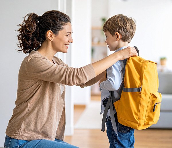 Caregiver helping young child with backpack, representing difficulty with transitions or separation from familiar routines or people.