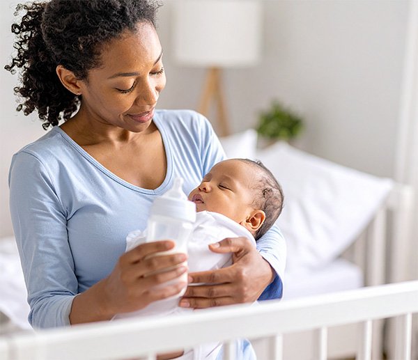 Caregiver feeding infant in nursery, symbolizing struggles with sleep, feeding, or daily routines addressed through early assessment.